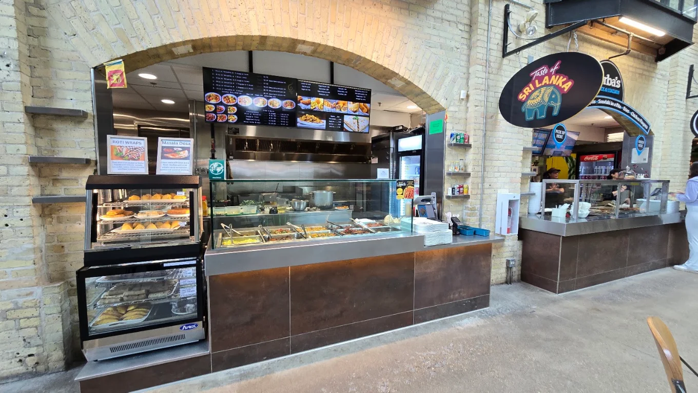 Taste of Sri Lanka counter inside The Forks Market, Winnipeg — hot curry counter and pastry display under the arched heritage brickwork